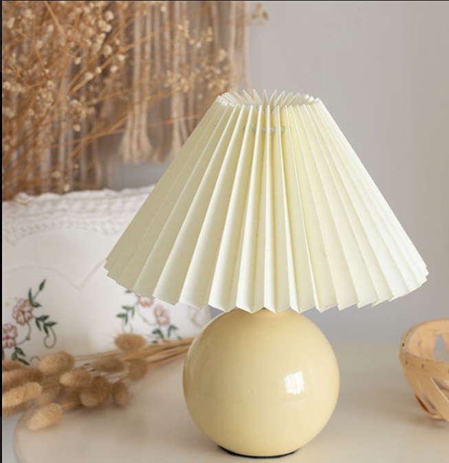 Yellow table lamp with pleated shade on a surface with decorative elements.